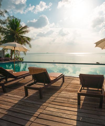 A serene beach scene with sun loungers, umbrellas, and a view of the ocean under a partly cloudy sky at sunset.