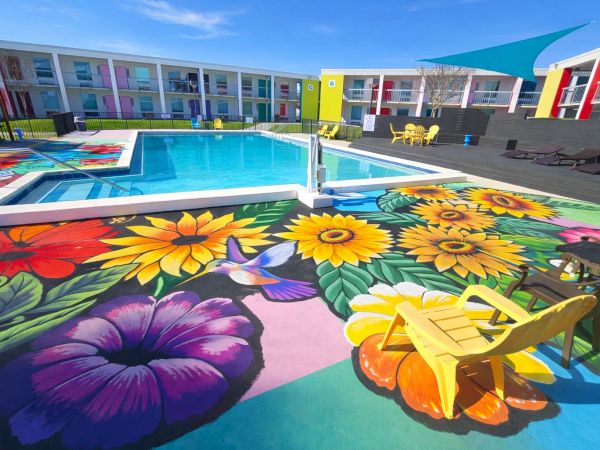 Colorful hotel pool area with bright sunflower and flower murals, sun loungers, and a turquoise pool under a blue sky.