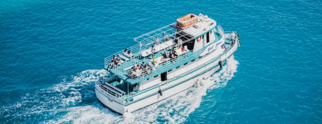 A small white motorboat cruising on clear blue water, leaving a frothy wake behind as it glides along.