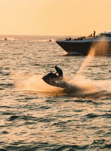 A person riding a jet ski on the water at sunset, with a boat in the background spraying a spray of water. end.