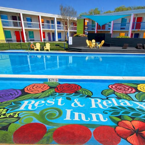 A colorful indoor pool area with playful, cartoon-like characters on the floor; cartoon barriers, bright slides, and seating around the water.
