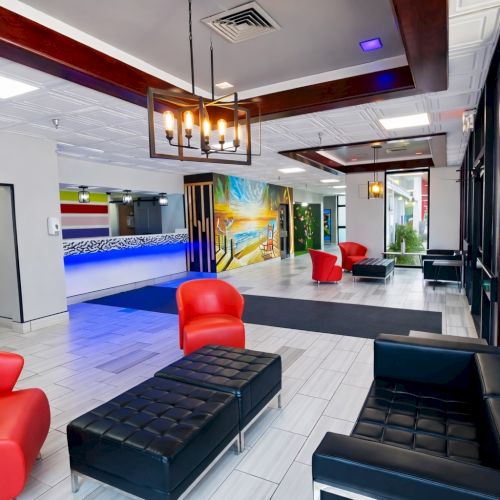 A modern lounge area with black and red seating, white tile floor, mirrored walls, and a bright reception desk in the background, cafe-style lighting.