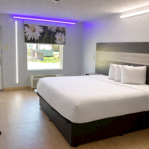 A modern hotel room with a large bed, stylish decor, a desk, a flat-screen TV, and warm lighting in a clean, minimalist space.